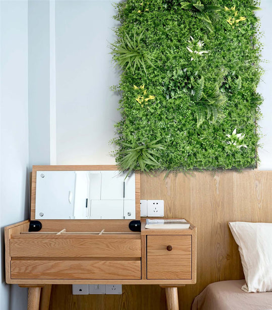 Lush green artificial plant wall panel above a modern wooden dresser in a stylish bedroom interior.