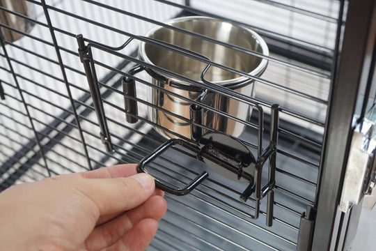 Hand adjusting food bowl holder in a durable bird cage showcasing quality design and ease of access.