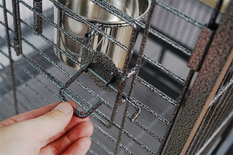 Hand holding the secure latch of a durable wrought iron bird cage with removable stainless steel bowl.