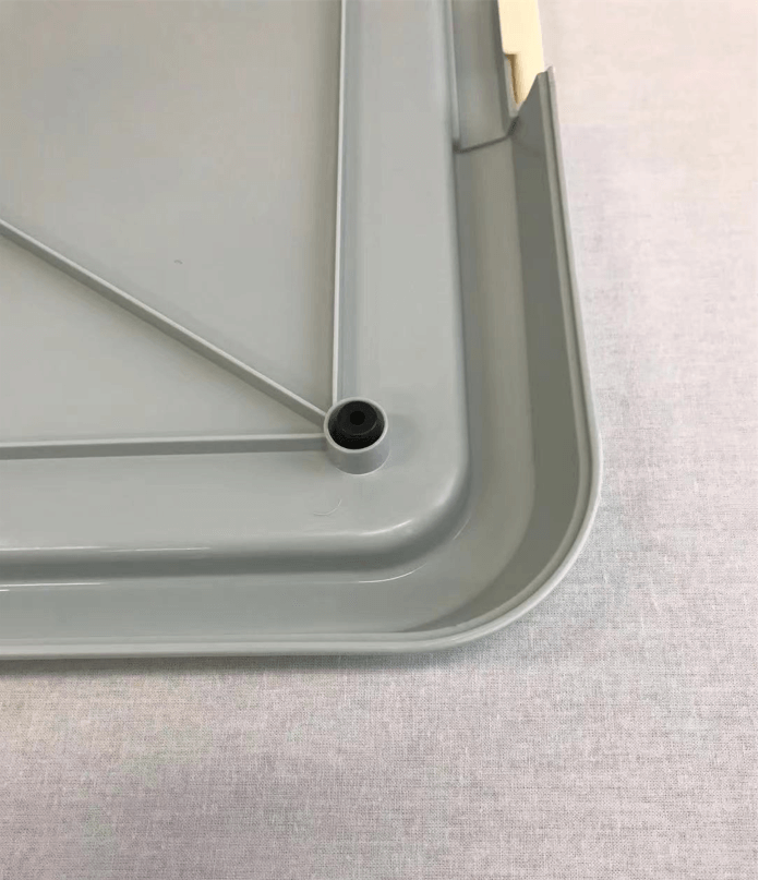 Close-up of the corner of a grey dog potty training tray with drainage hole and detailed design.