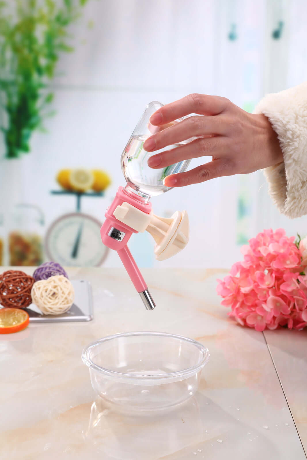 Hand holding a pink pet water bottle above a bowl, showcasing its no-drip design for small animals.