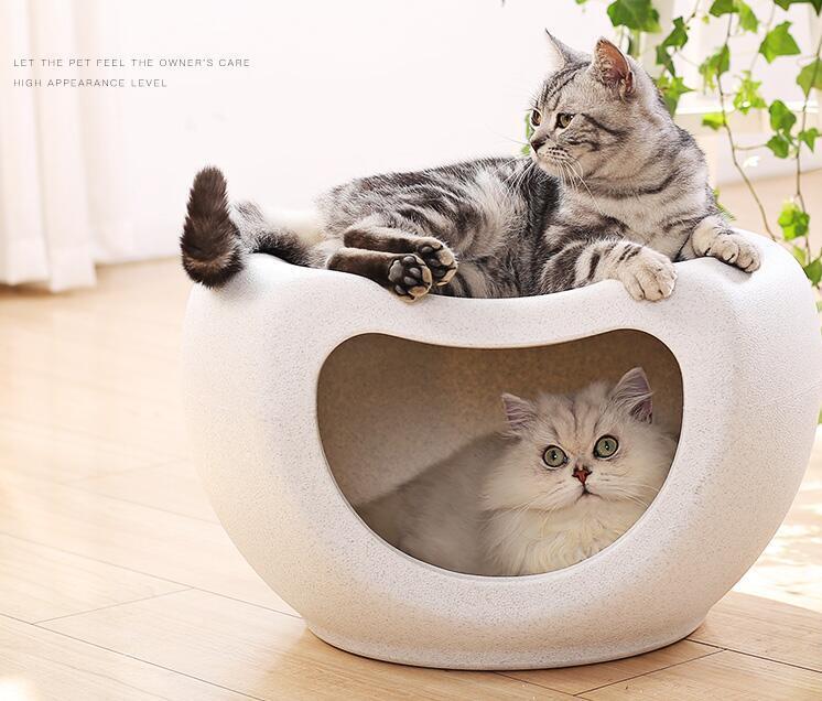 Two cats lounging in a stylish white pet pod, one inside and one outside, showcasing a cozy and modern design.