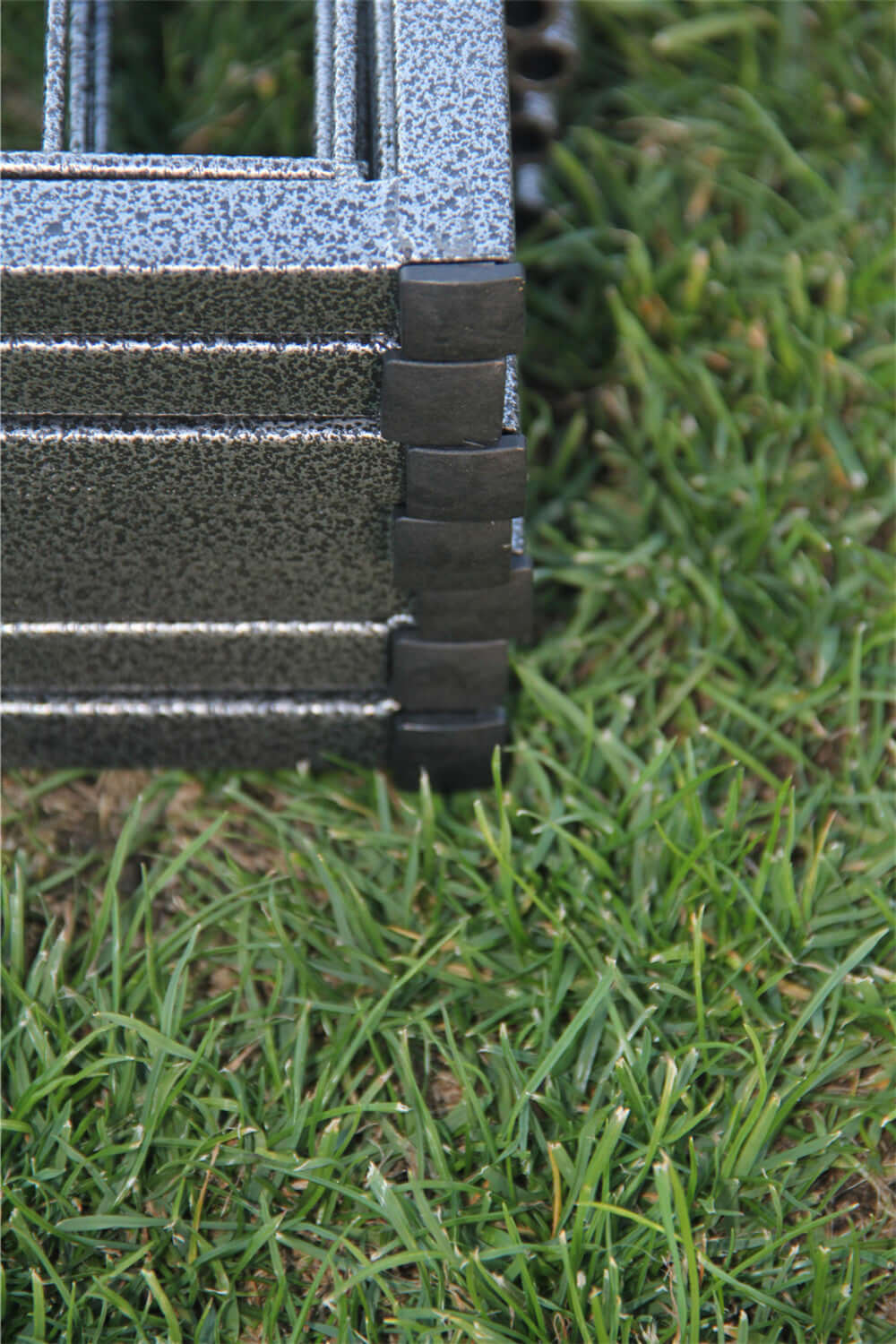 Close-up of the heavy-duty metal fence connection on a pet exercise playpen on green grass.