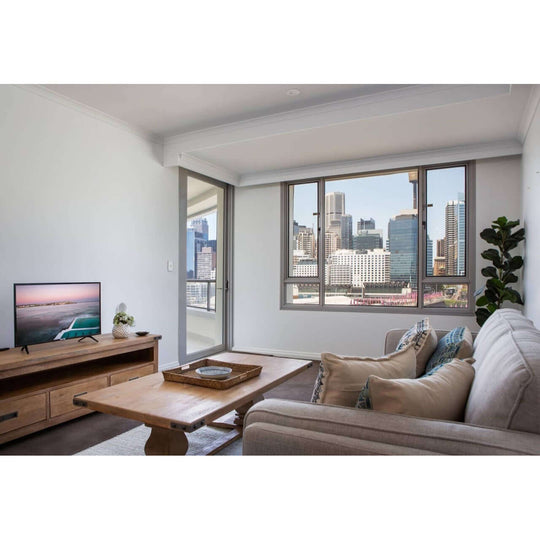 Modern living room with a TV unit, coffee table, cozy sofa, and city view through large windows.