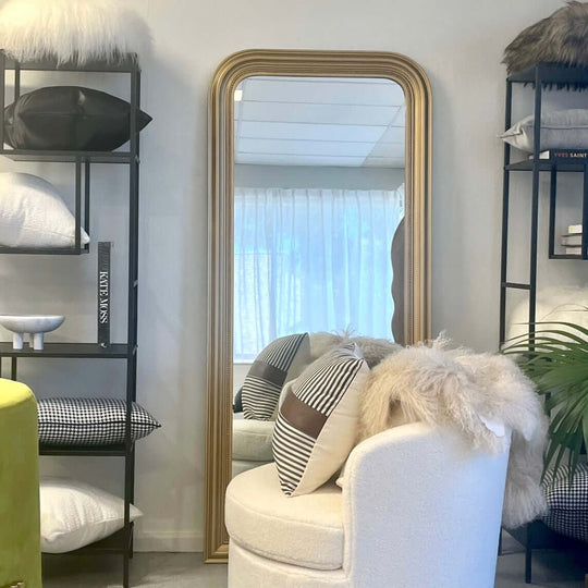 Large golden-framed full-length mirror reflecting a stylish interior with cushions and decor accents.