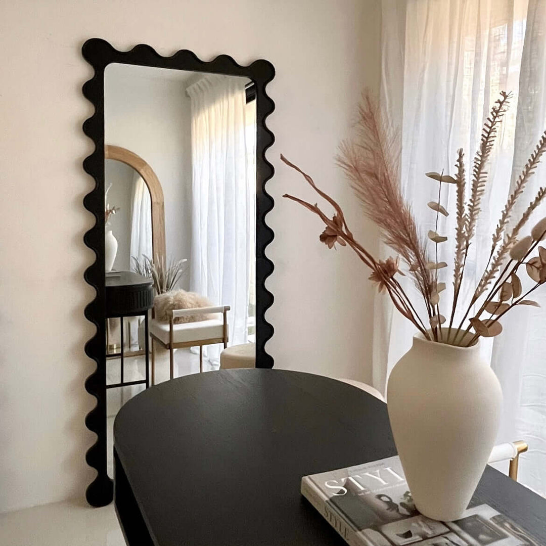 Large black scalloped mirror reflecting stylish decor with vase and light curtains, perfect for affordable and quality home styling.