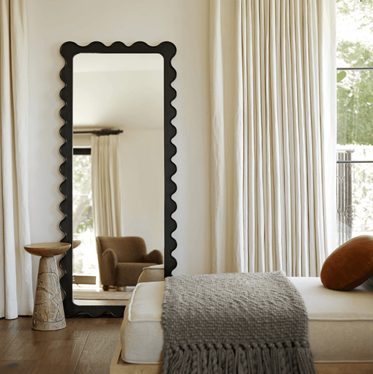 Tall black scalloped mirror in modern room with natural light, stylish decor, and cozy furnishings.