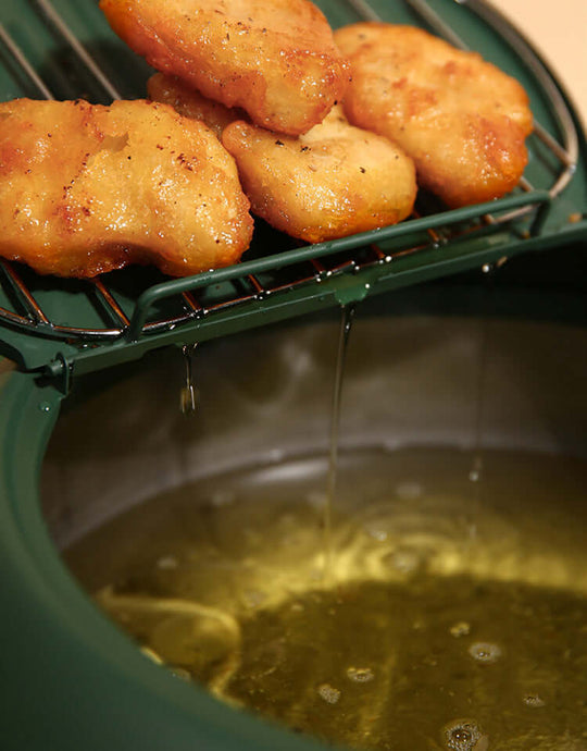 Crispy fried snacks draining on a rack above hot oil in a Justcook tempura fryer pot. Affordable quality DIY cooking.