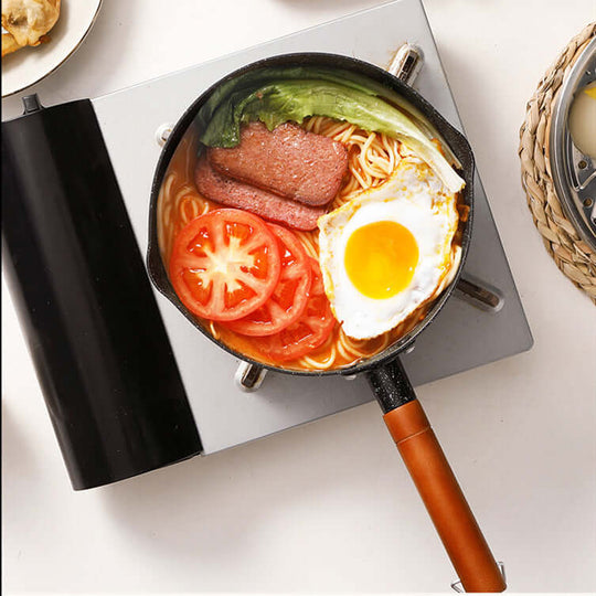 Delicious meal in Justcook Xueping pot with noodles, tomatoes, egg, and vegetables on burner. Affordable and durable cookware.