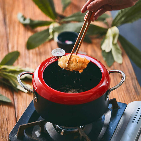 Justcook 20cm double handle fryer pot in use with a piece of fried food being lifted via chopsticks, showcasing its quality and design.