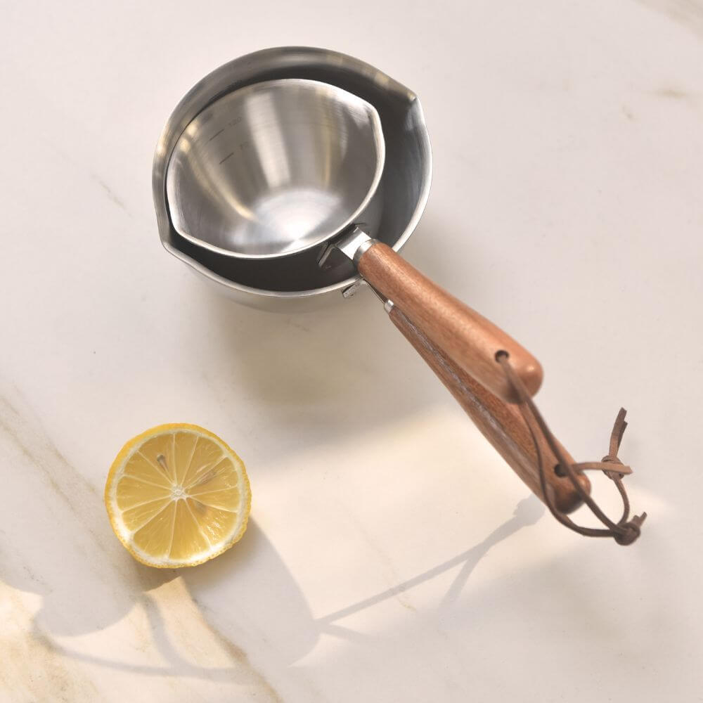 Kylin 304 stainless steel oil poured pot with wood handle beside a lemon slice on a marble surface. Affordable kitchen tool for stylish cooking.