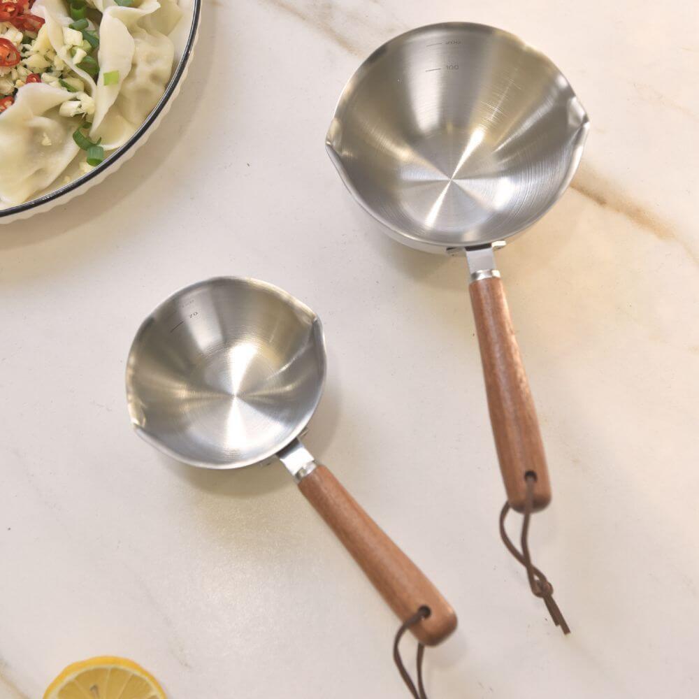 Stainless steel measuring cups with wooden handles on a marble countertop, ideal for cooking and DIY tasks.