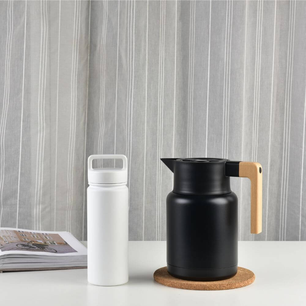 Sleek black Kylin vacuum jug and white bottle on a table with a cork coaster and magazines in a modern setting.