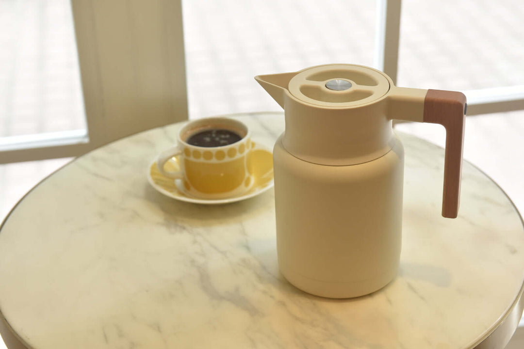 Kylin 304 stainless steel Japanese vacuum jug beside a coffee cup on a marble table, showcasing quality and stylish design.