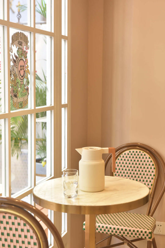 Kylin 304 stainless steel Japanese vacuum jug on a table near a glass, with a stylish café backdrop.