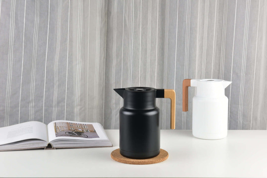 Kylin 304 stainless steel Japanese vacuum jug in black and white on a table with a book and cork coaster.