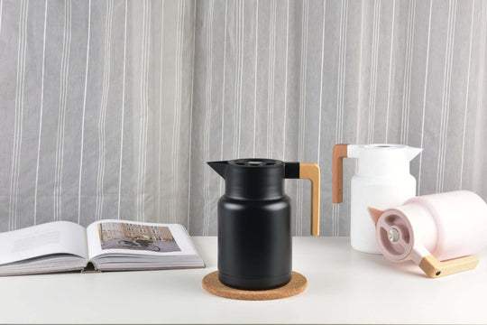 Modern black jug with wooden handle, white jug beside it, and open book on table, showcasing stylish beverage containers.