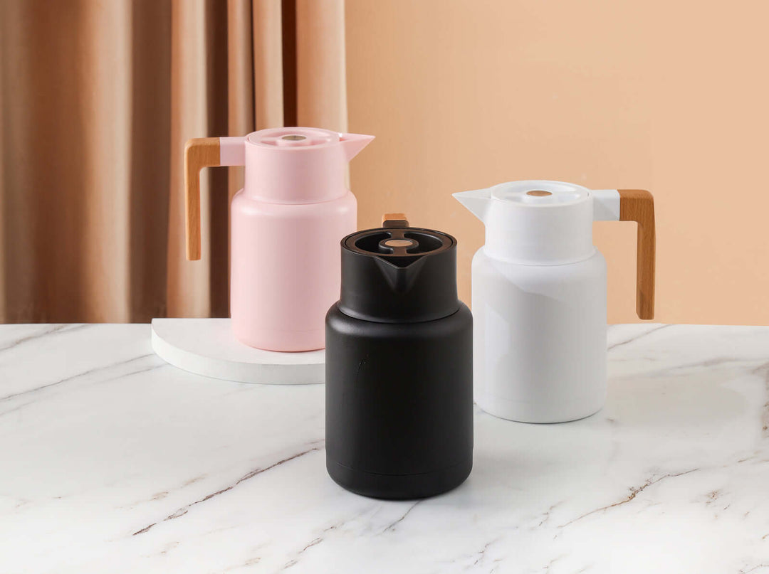 Stylish Kylin stainless steel vacuum jugs in pink, black, and white with wooden handles on a marble surface.