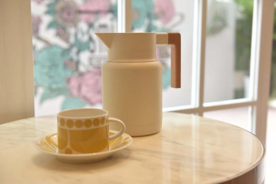 Elegant Kylin 304 stainless steel Japanese vacuum jug beside a yellow patterned cup on a marble table.