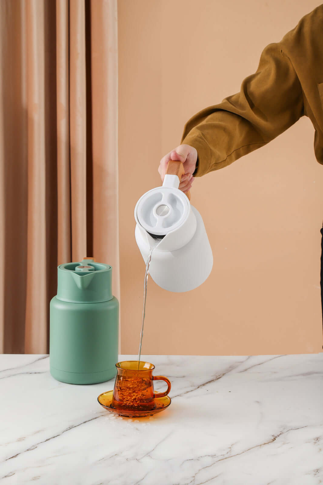 Person pouring from Kylin 304 stainless steel Japanese vacuum jug into amber glass cup on a marble table.