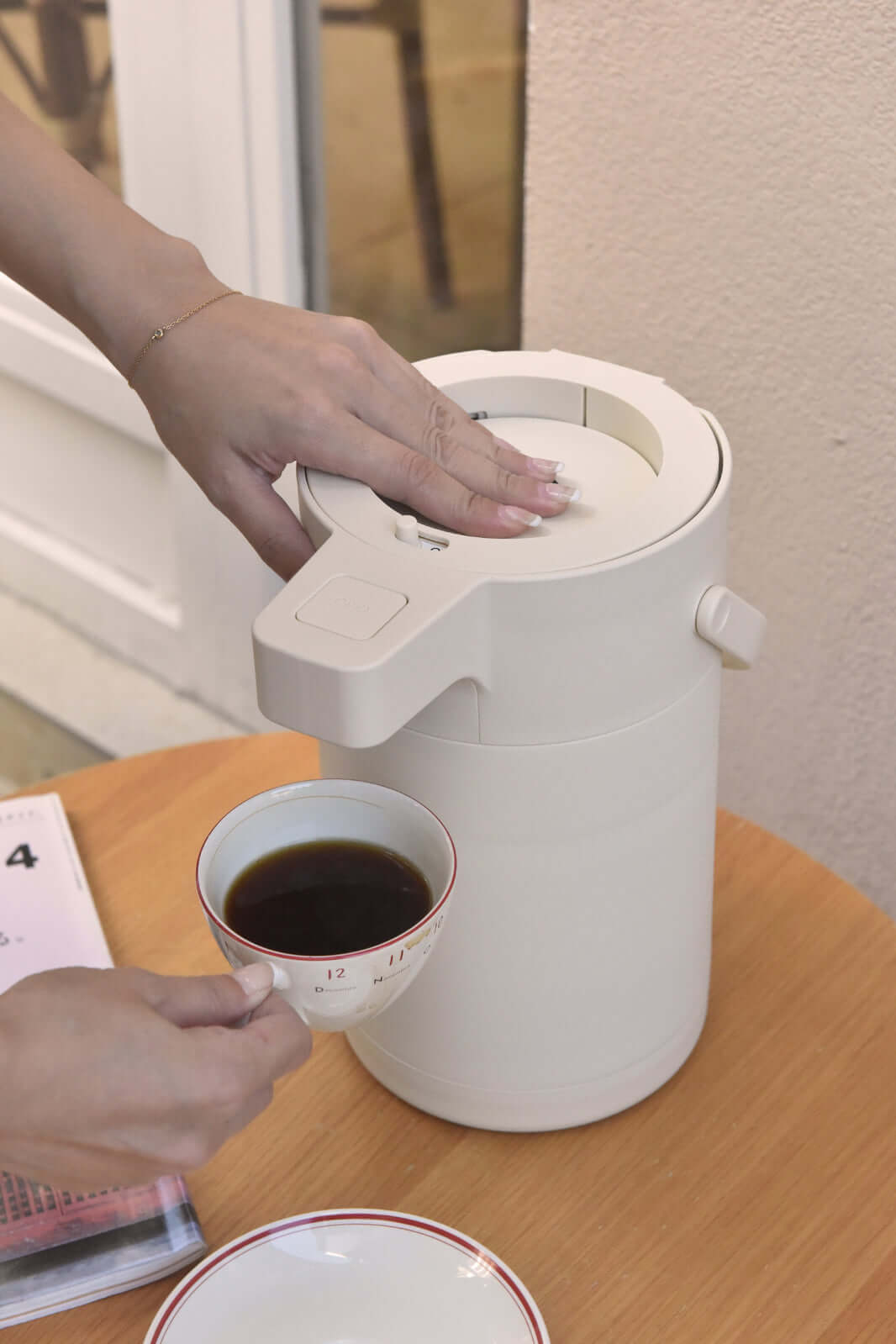 User pouring coffee from Kylin 304 stainless steel air press pot beverage dispenser on a wooden table.