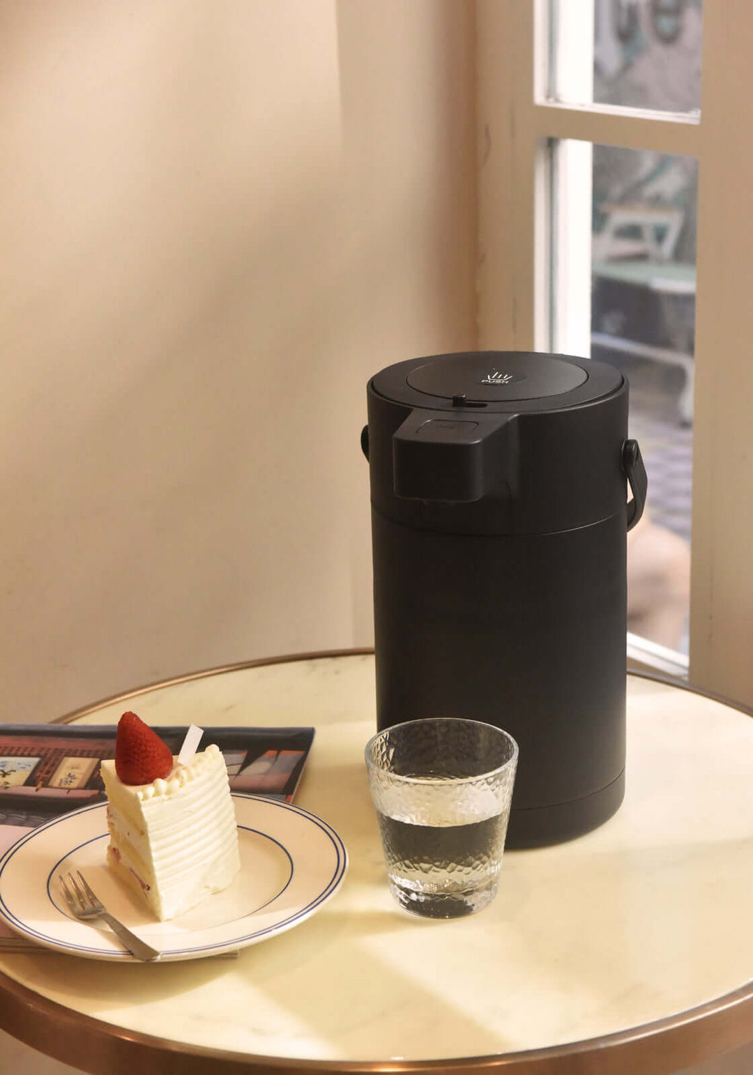 Kylin 2.5L stainless steel air press pot dispenser with dessert and glass of water on a table near a window.