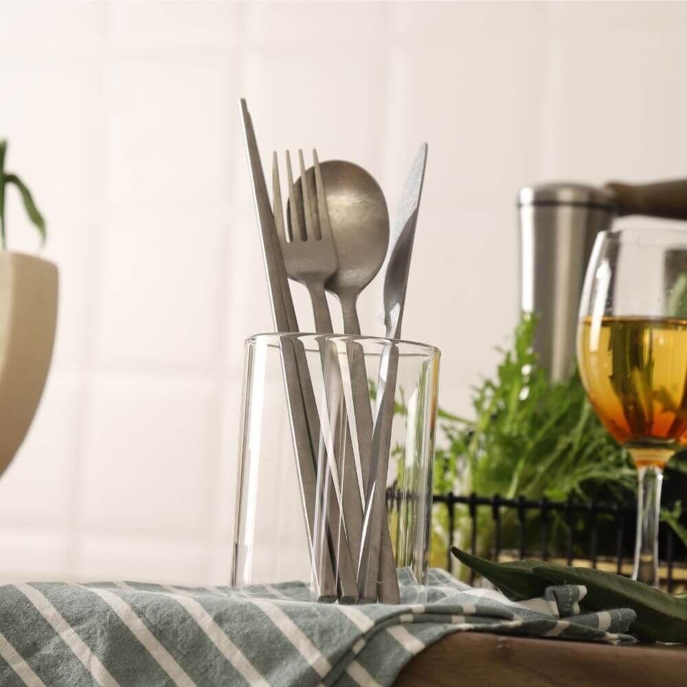 Elegant stainless steel cutlery displayed in a glass, featuring forks and spoons, perfect for stylish dining settings.