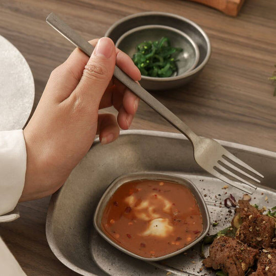 Hand holding Kylin 304 stainless steel classic fork in snow gray over a plate of food, showcasing affordable quality dining.