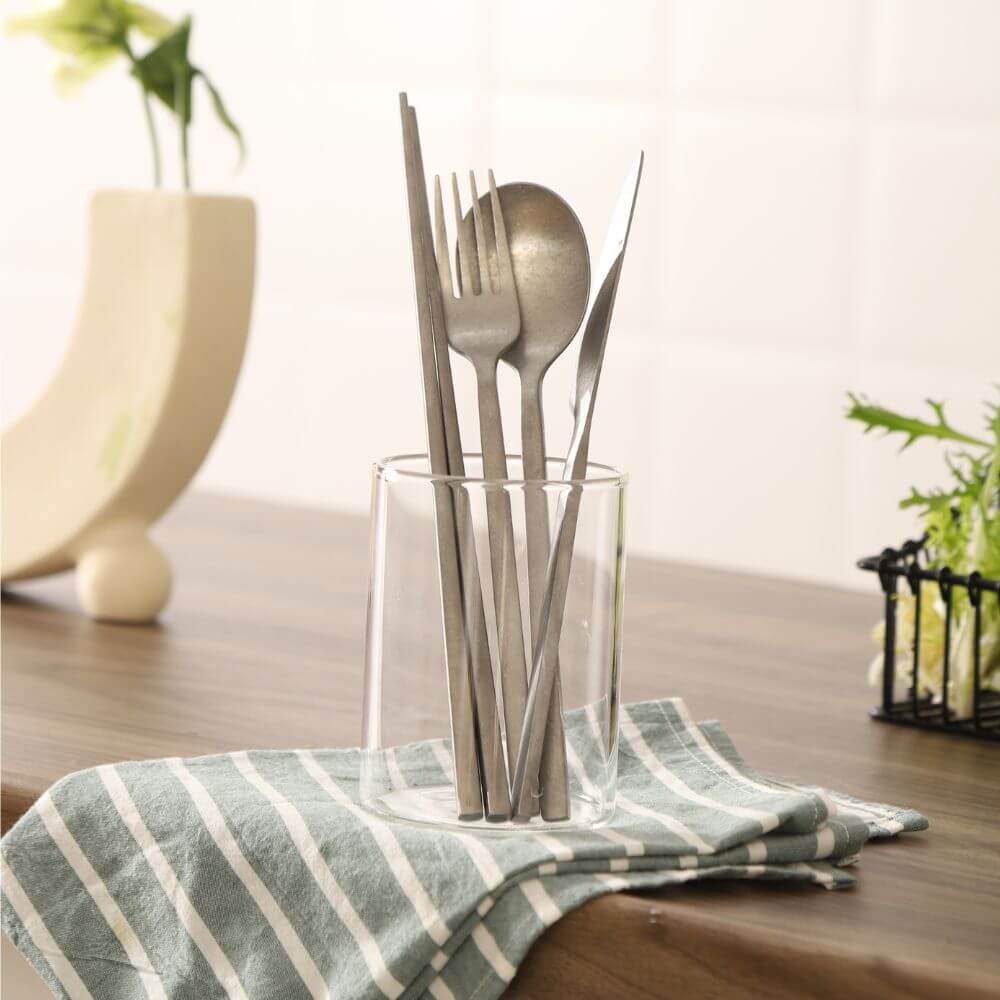 Stylish stainless steel cutlery set displayed in a glass on a striped cloth, perfect for affordable and quality dining experiences.