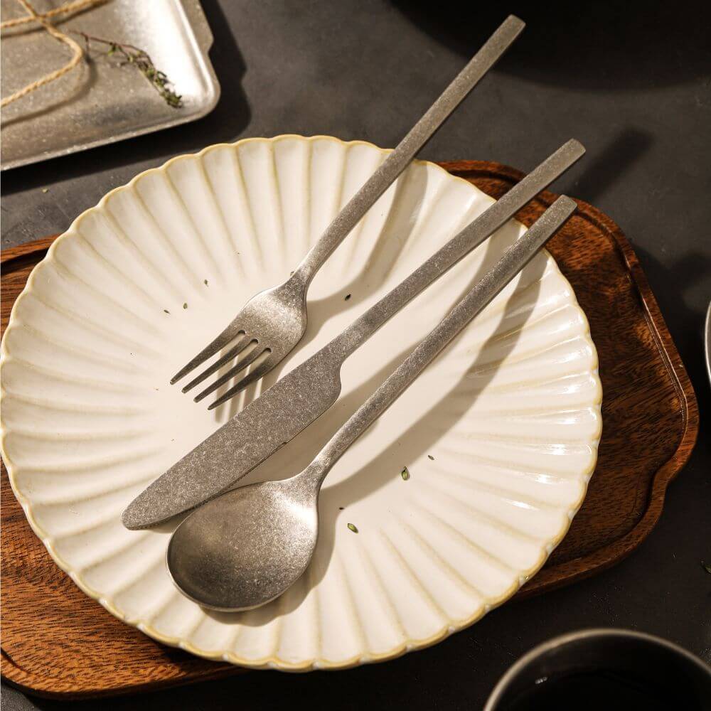 Elegant snow gray flatware on a decorative plate, featuring a spoon, knife, and fork for stylish dining.