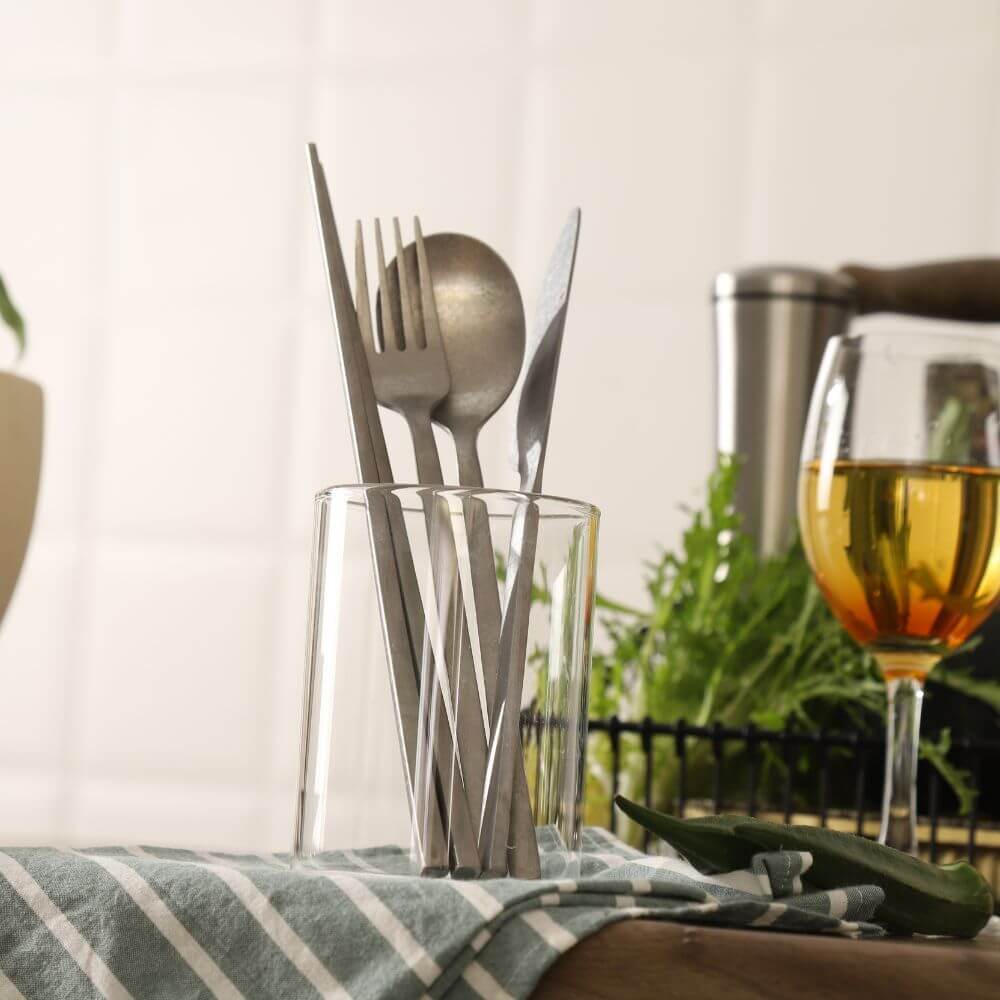 Elegant dining utensils in a glass holder, featuring silver cutlery and a wine glass, set on a striped tablecloth.