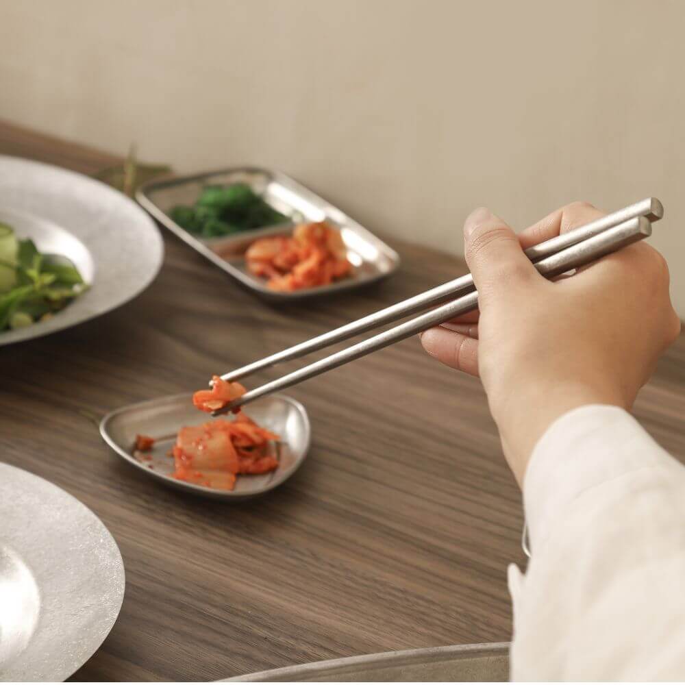 Hand using Kylin stainless steel chopsticks to pick up food from a stylish plate, showcasing elegance and quality dining.