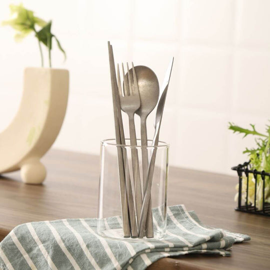 Elegant stainless steel utensils in a glass holder on a striped napkin, perfect for dining and DIY table settings.