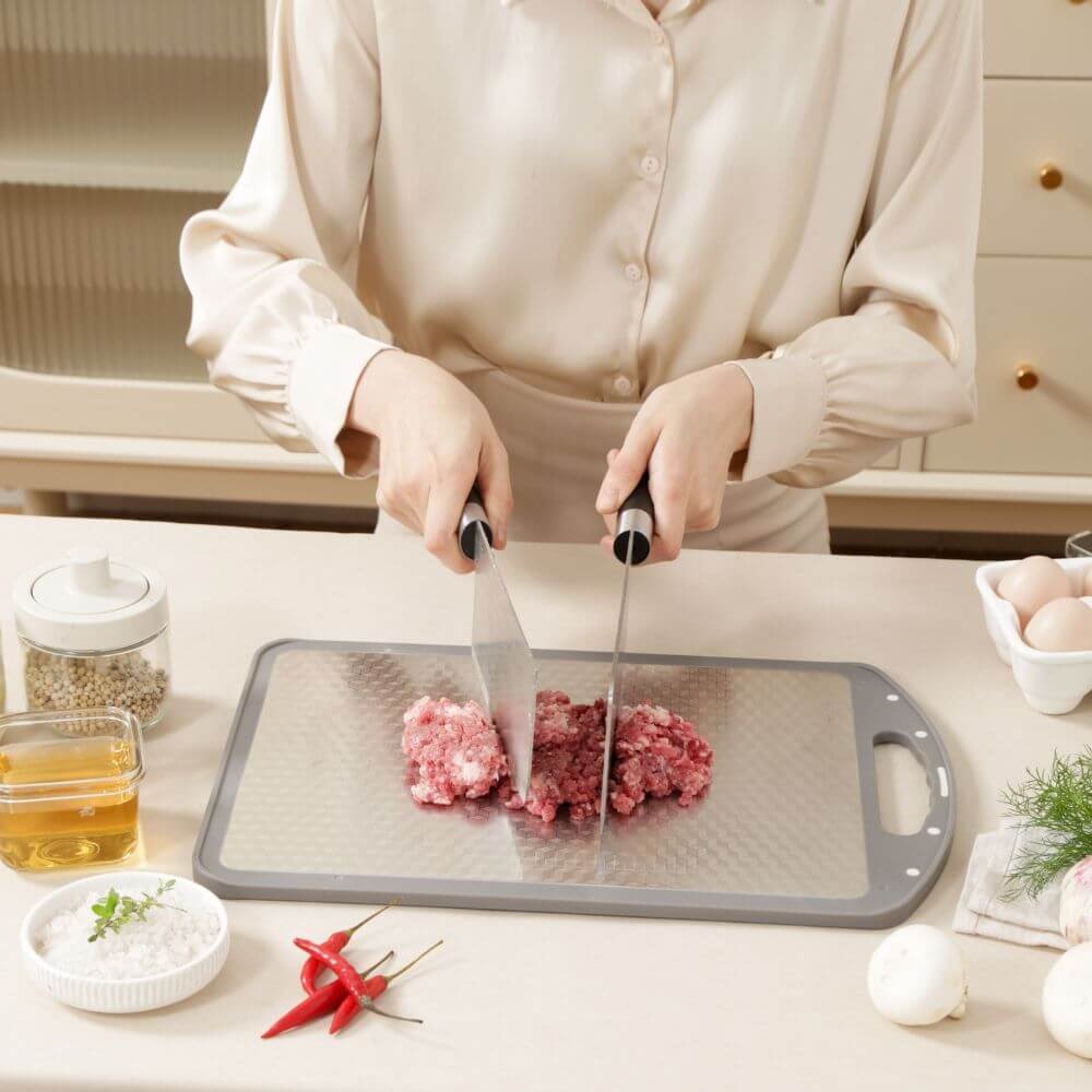 Woman chopping meat on Kylin 316 stainless steel double side cutting board in a modern kitchen setting.