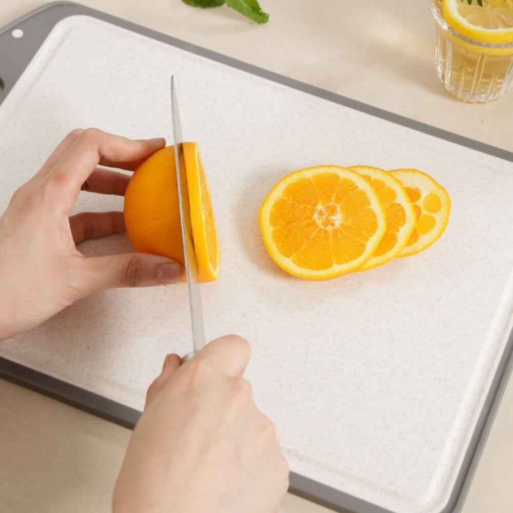 Hand slicing an orange on a Kylin stainless steel double-sided cutting board for quality kitchen use.