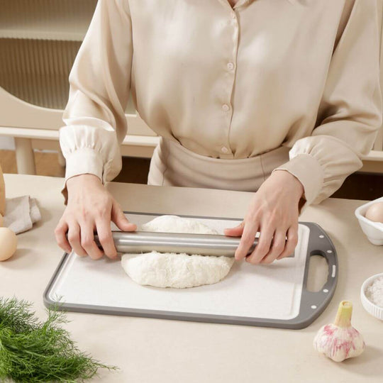 Person using a rolling pin on dough on a cutting board in a cozy kitchen setting.