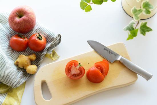 Yanagi Japanese kitchen chef knife on a wooden cutting board with fresh tomatoes and an apple.