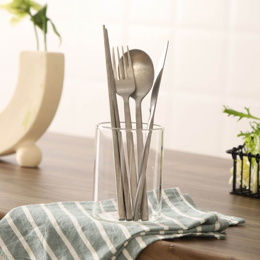 Stainless steel cutlery set displayed in a glass container on a striped cloth, ideal for stylish dining.