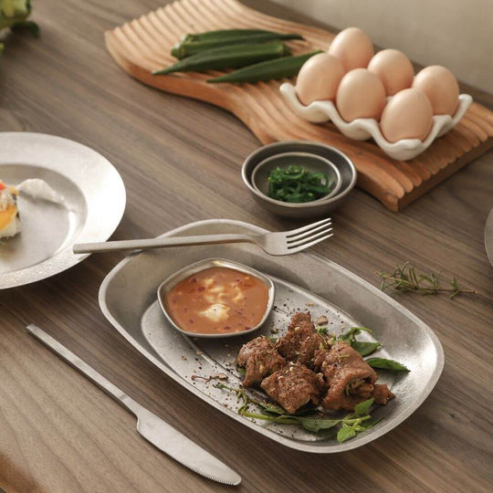 Elegant table setting featuring a plated beef dish, sauce, and fresh ingredients with steak knife and fork on a wooden table.