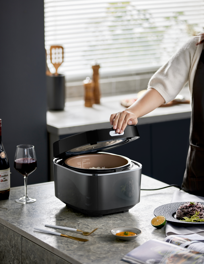 Person operating BEAR 4 Litre Intelligent Power Heating Rice Cooker in modern kitchen, next to wine glass and food.