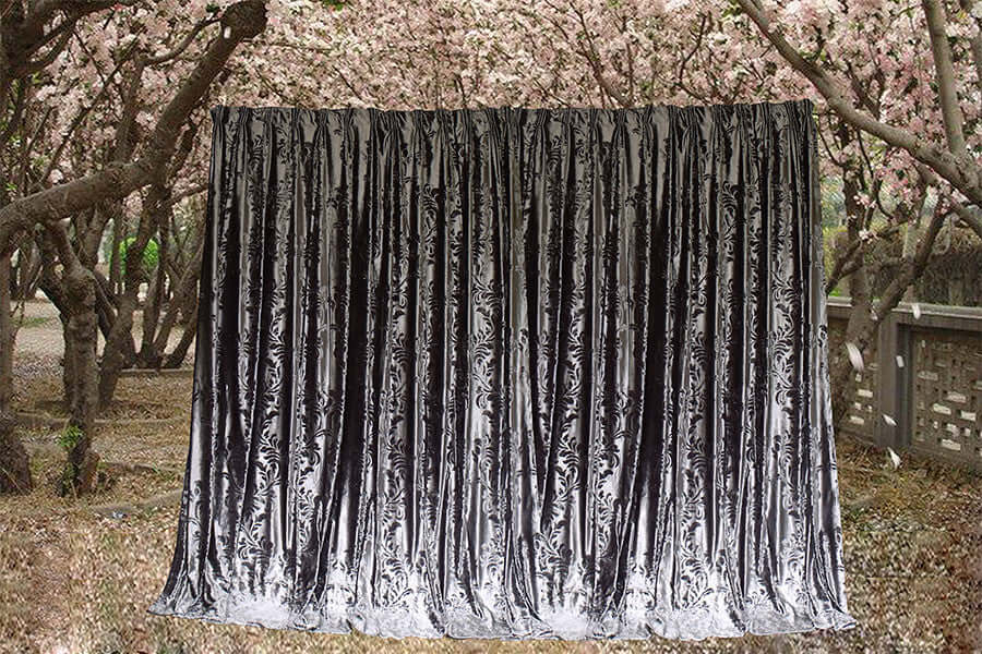 Large silver grey velvet curtains hanging among blooming trees, showcasing luxurious texture and elegant design.