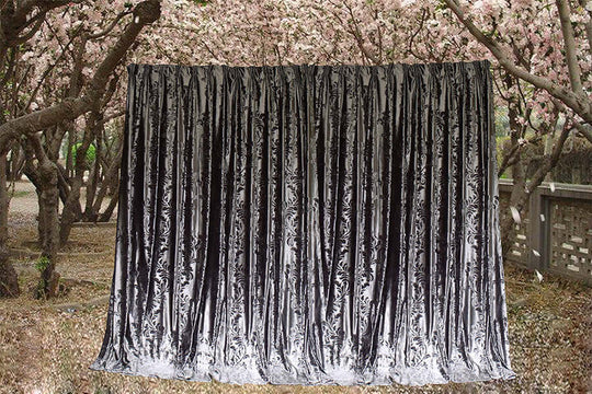 Large silver grey velvet curtains hanging among blooming trees, showcasing luxurious texture and elegant design.