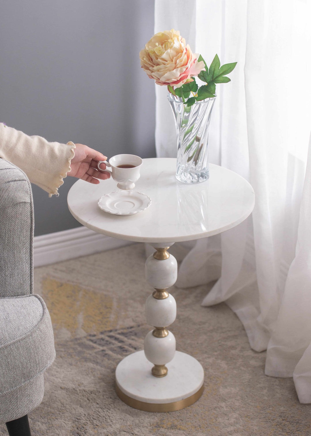 Handcrafted pebble marble and aluminum side table with coffee cup and flower vase in elegant living room setting.