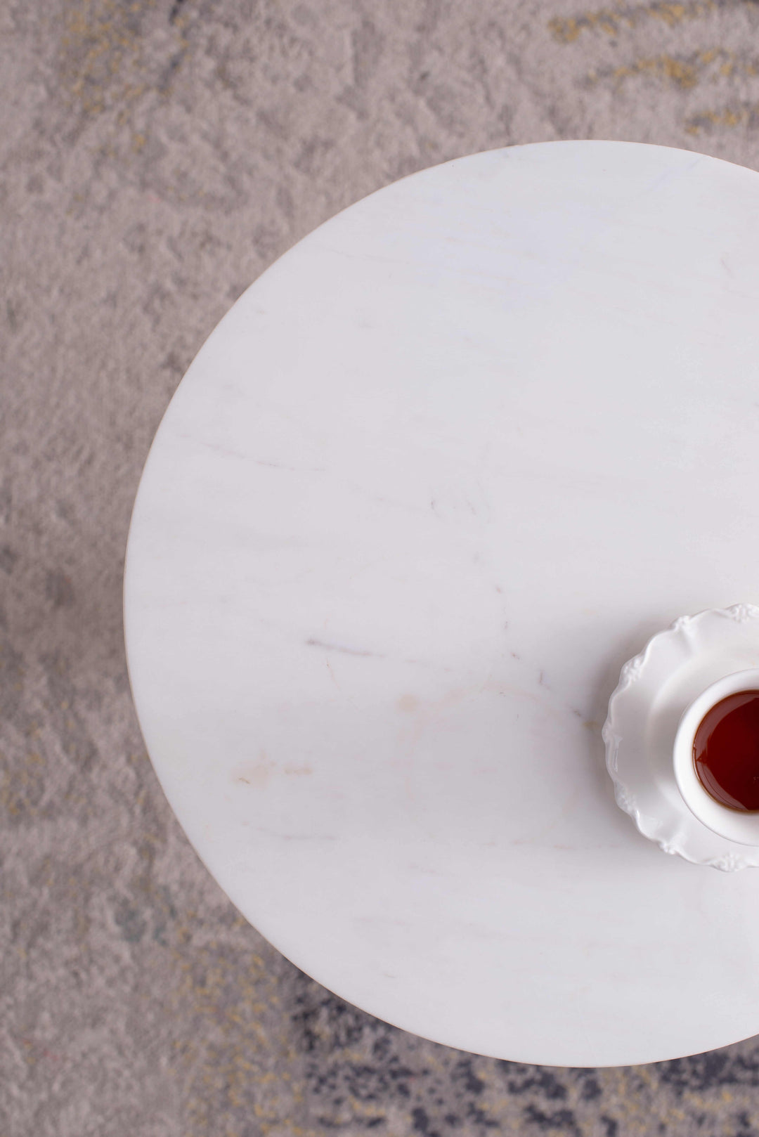 Top view of a round pebble marble side table with a white dish holding tea, set on a textured rug.