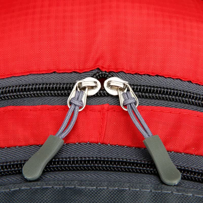 Close-up of the zippers on a red waterproof hiking backpack, showcasing quality craftsmanship and durable materials.