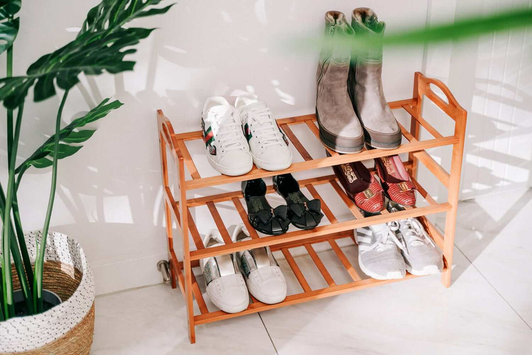 Bamboo 3-tier shoe storage rack displaying various shoes in a modern home setting with greenery and a decorative basket.