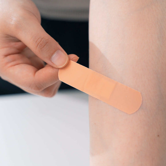 Applying a beige adhesive bandage on a person's arm, showcasing first aid essentials from the mini emergency kit.