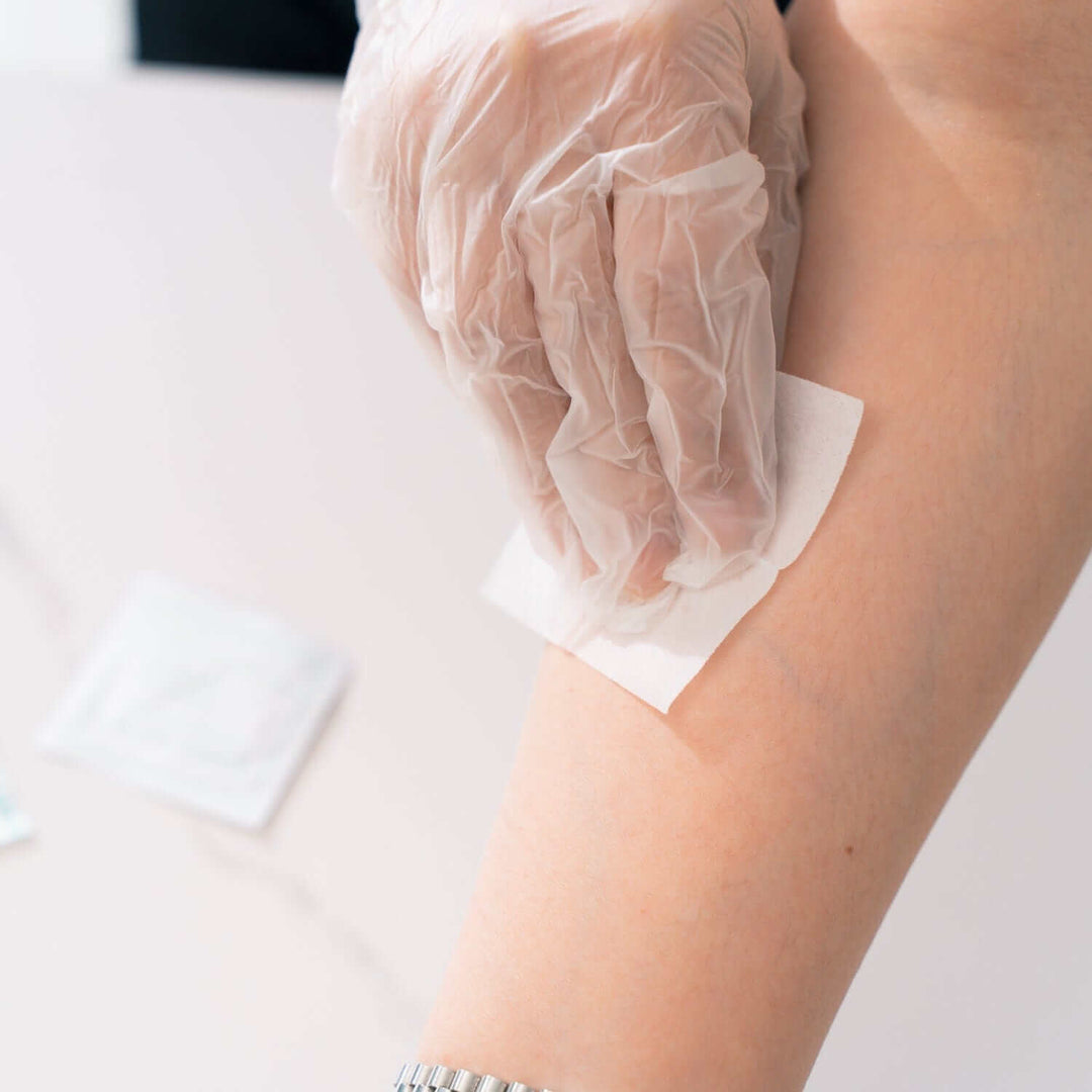 Person applying a sterile bandage with gloved hands during first aid treatment.