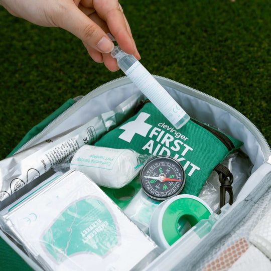 Close-up of a hand retrieving a gel from a green first aid kit on grass, showcasing quality emergency supplies.