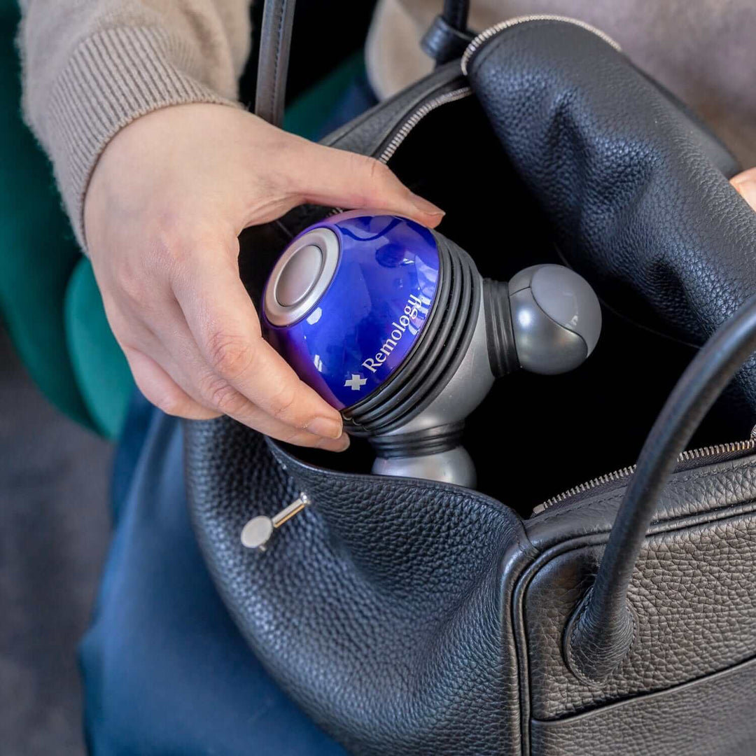 Person placing Remology Mini Therapy Handheld Massager into a stylish bag, showcasing its portability and convenience.